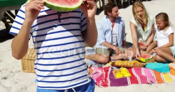 男孩一边吃西瓜一边家人坐在沙滩上视频的预览图