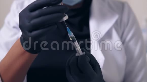 一位戴着黑色手套和口罩手里拿着医用注射器的无法辨认的专业医生的特写镜头视频的预览图