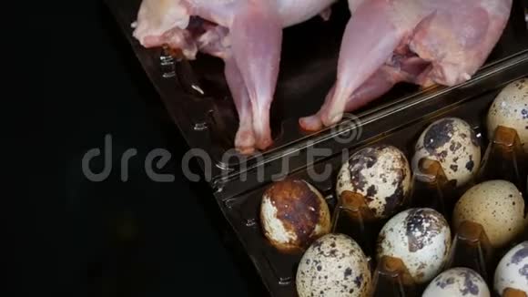 鹌鹑的新鲜肉在黑色背景的鹌鹑蛋旁边的塑料棕色托盘中旋转视频的预览图