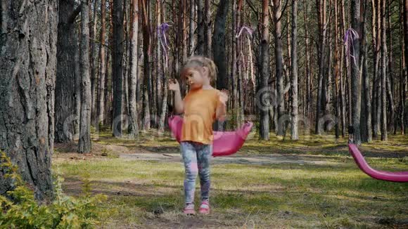 可爱的女孩在森林里玩着五颜六色的秋千视频的预览图