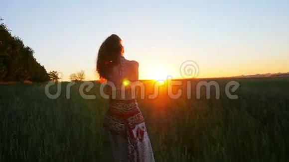 年轻女子在日出时快乐地跑过绿色的田野慢动作视频的预览图