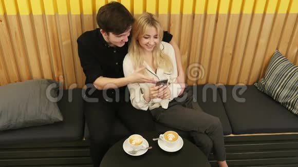 可爱的一对夫妇在咖啡馆里看智能手机视频的预览图