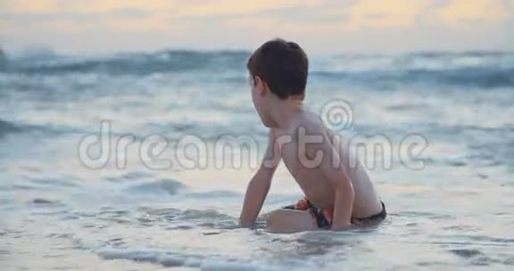 日落时坐在海滩上的孩子视频的预览图