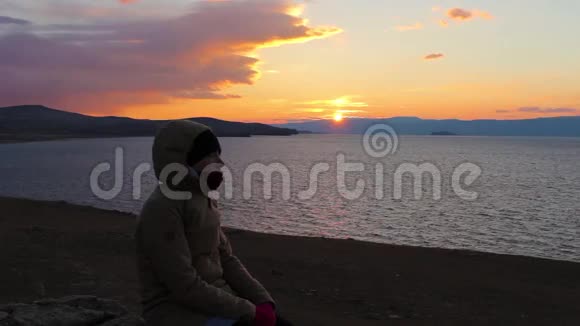女孩坐在海边望着远处美丽的日落视频的预览图