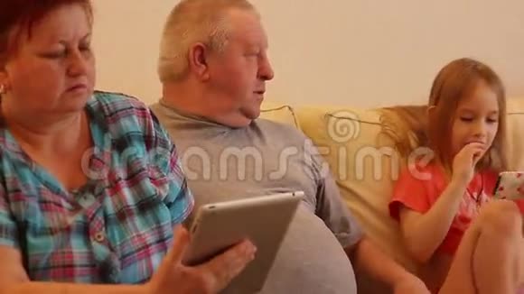 老人夫妇和他们的孙子在客厅里使用数码平板电脑视频的预览图