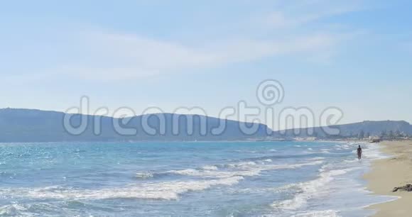 波浪降落在沙滩上女人走路清澈的蓝水视频的预览图