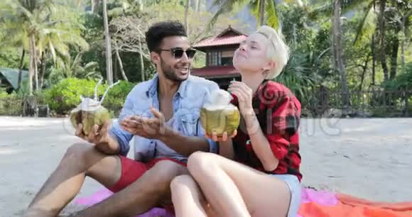 沙滩上的情侣饮料椰子鸡尾酒棕榈树下的谈话欢乐的男人和女人的游客交流视频的预览图