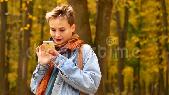 秋天落叶背景下带着手机的女孩的肖像一个年轻的女人正在调查视频的预览图
