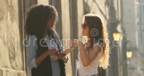 在阳光明媚的日子里两位美丽的多元文化学生交谈的景观视频的预览图