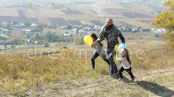 父亲带着两个女儿带着气球在草地上奔跑视频的预览图