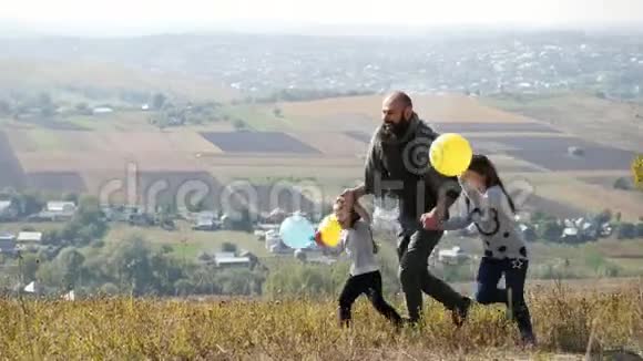 父亲带着两个女儿带着气球在草地上奔跑视频的预览图