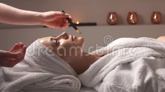 专业美容师在美容院将化妆面具涂在女性脸上女人在水疗中心做美容视频的预览图