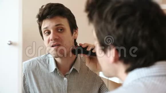 机刮脸发年轻英俊的男人用电动修剪机干剃须刀视频的预览图