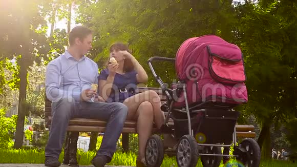 爸爸和妈妈吃冰淇淋和婴儿车一起在公园散步暑假全家放假视频的预览图