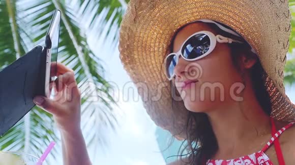 女士戴着太阳镜和帽子在暑假的海滩上使用电话应用程序慢动作1920x1080视频的预览图