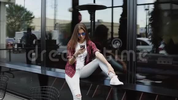 一位漂亮的女士戴着名牌眼镜穿着休闲装在商店橱窗附近使用手机视频的预览图