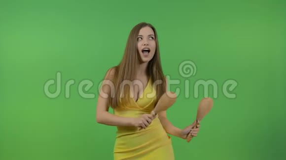 年轻美丽的女孩长发与马拉卡斯跳舞有趣和快乐在绿色的背景上视频的预览图