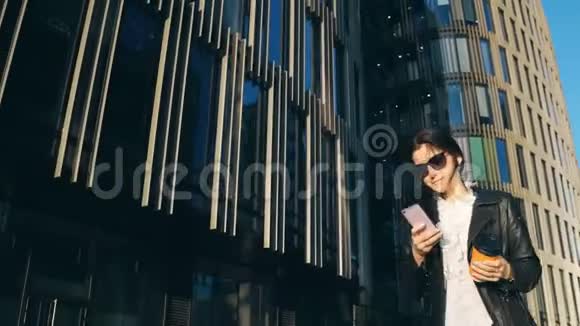 年轻漂亮的女商人带着一杯咖啡带着智能手机在城市里带着办公楼视频的预览图