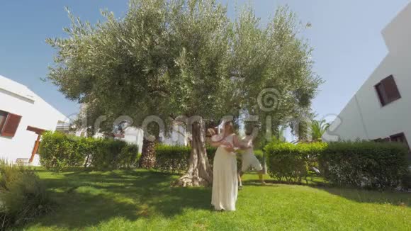 绿色花园里有一棵大橄榄树的快乐父母和孩子视频的预览图