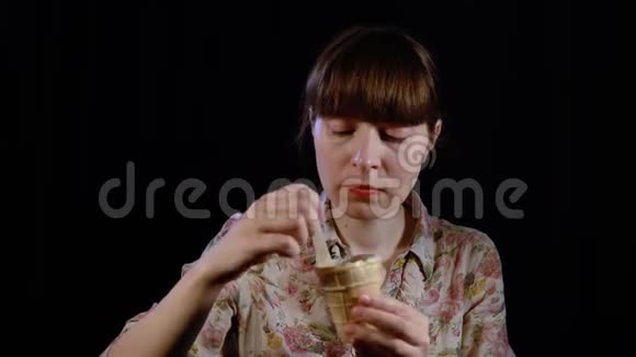 年轻的女人正在用勺子在黑色的背景上吃冰淇淋视频的预览图