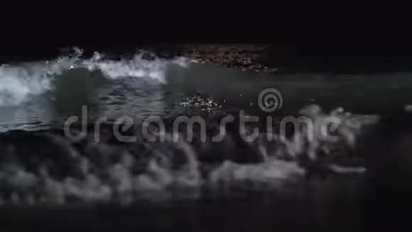 夜晚黑暗的泡沫海浪冲刷着海滨视频的预览图