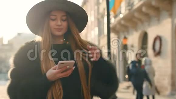 美丽的黑发女人戴着灰色帽子站在拥挤的城市街道上用她的手机发短信视频的预览图