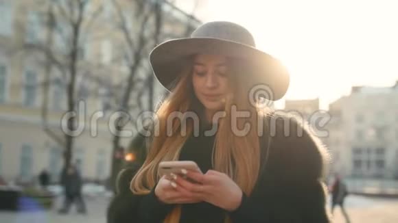 美丽的黑发女人戴着灰色帽子站在拥挤的城市街道上用她的手机发短信视频的预览图