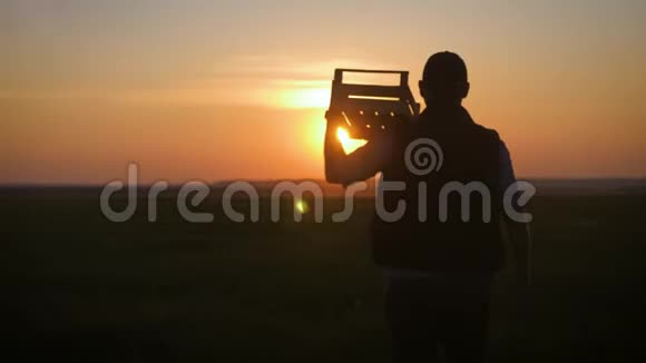 日落时分一位年轻的农民带着一个装有新鲜蔬菜的木箱在田野上散步健康饮食秋天视频的预览图