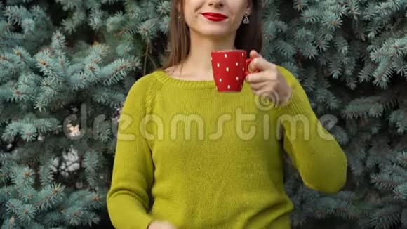 女人拿着一个舒适的红色杯子在松枝的背景下视频的预览图