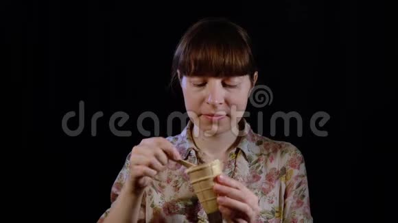 年轻的女人正在用勺子在黑色的背景上吃冰淇淋视频的预览图