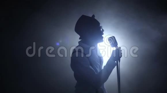 歌手一半的营业额在烟雾和白光唱在麦克风黑色背景剪影慢慢视频的预览图