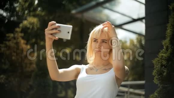 年轻的金发女人看着智能手机上的反光她的头发用手机做镜子视频的预览图