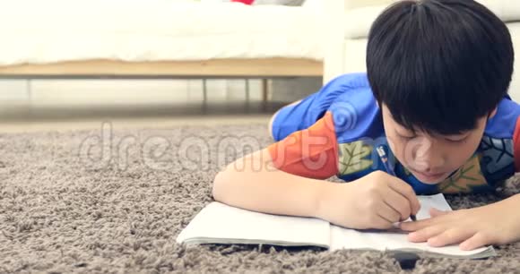 可爱的亚洲男孩在地板上休息微笑着在家做作业视频的预览图