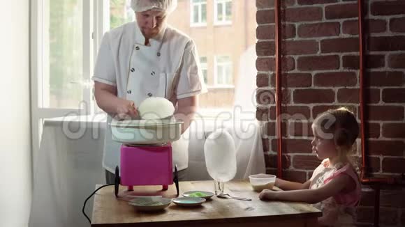 一个男厨师在一台特殊的机器上为一个可爱的小女孩做棉花糖视频的预览图