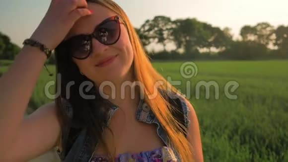 美丽的年轻女孩直长发在风中发展日落时站在田野里慢动作视频的预览图