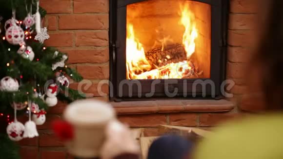 在圣诞节的时候一个女人坐在壁炉旁坐在摇椅上端着杯子放松视频的预览图