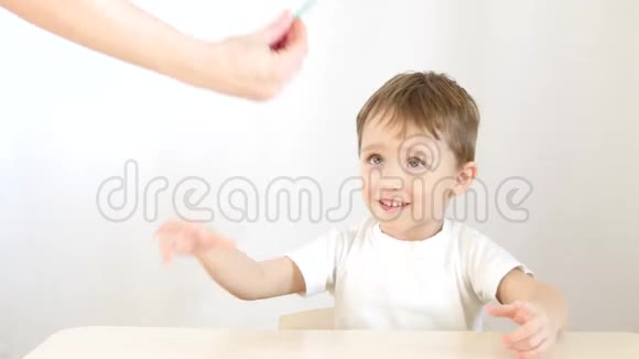 小男孩微笑着吃棒棒糖坐在白色背景的桌子旁视频的预览图