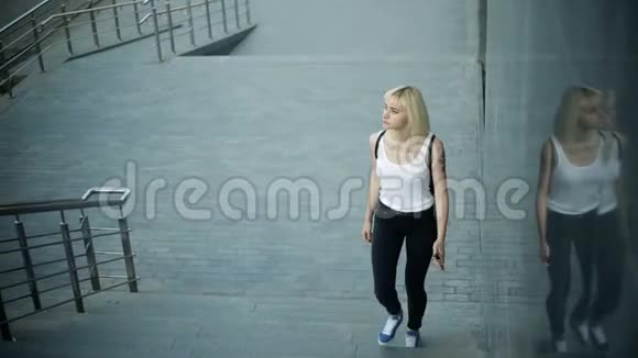 年轻的金发女人爬上城市的楼梯向摄像机移动然后经过视频的预览图