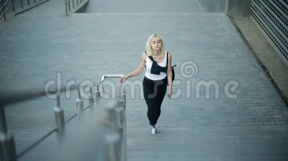 年轻的金发女人爬上城市的楼梯向摄像机移动然后经过视频的预览图