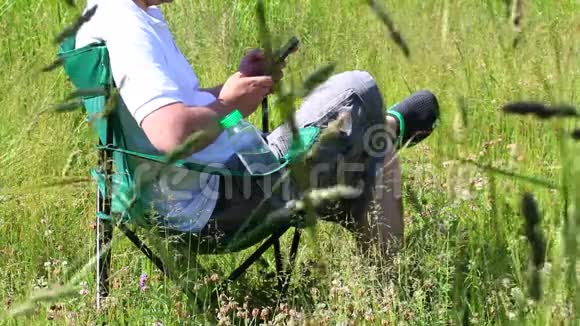 一个男人坐在折叠的野餐椅上在智能手机里玩然后他站起来离开视频的预览图