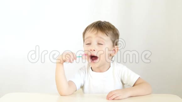 快乐的孩子微笑着吃棒棒糖坐在一张白色背景的桌子上视频的预览图