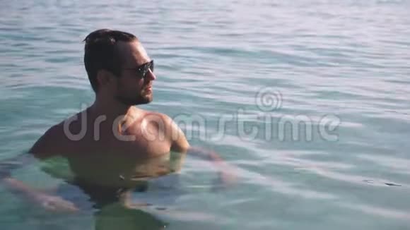 一个英俊的年轻人戴着墨镜在清澈的海水中放松视频的预览图