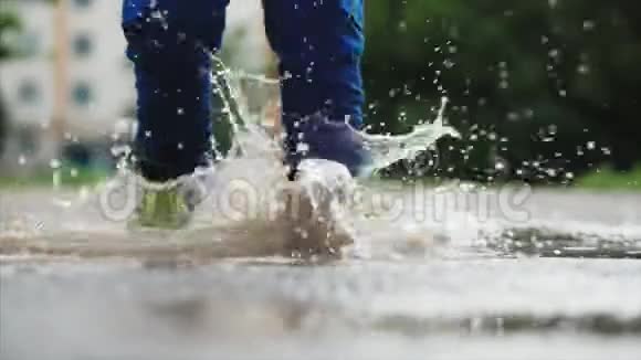 低角度特写无法辨认的孩子在雨后的夏天穿过水坑在水坑里奔跑的无忧无虑的孩子视频的预览图
