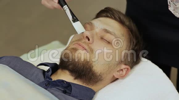 涂上奶油面膜按摩脸部和颈部有胡子的男人透明面具视频的预览图
