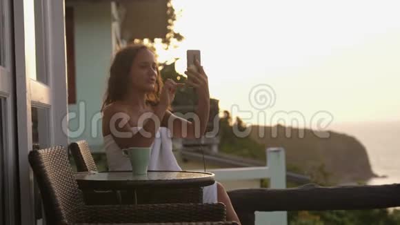 在日落时分年轻女子在酒店阳台上用智能手机进行视频聊天展示观看分享旅游体验视频的预览图