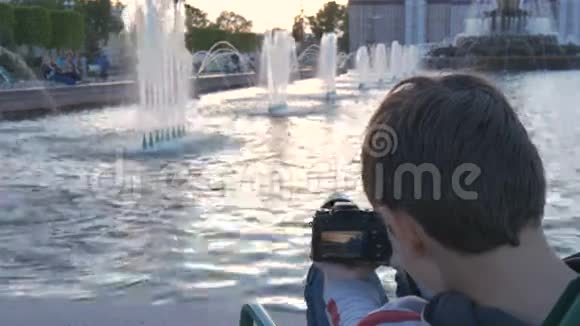 这个男孩是个十几岁的孩子坐在喷泉旁边的一个美丽的地方拍摄水溅的照片美丽的风景视频的预览图