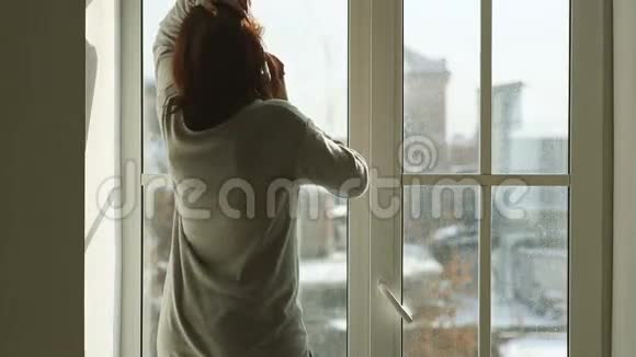 女人拿着智能手机站在窗户旁边视频的预览图