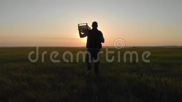 日落时分一位年轻的农民带着一个装有新鲜蔬菜的木箱在田野上散步健康饮食秋天视频的预览图