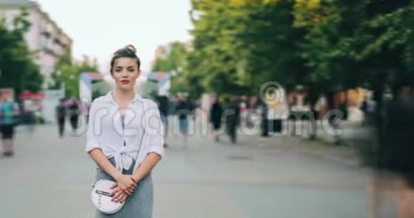 穿着现代服装的女孩看着摄像机站在城市街道上的时间流逝视频的预览图