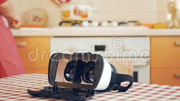 虚拟现实眼镜放在桌子上家庭主妇把胡萝卜放进炉子上的汤里视频的预览图